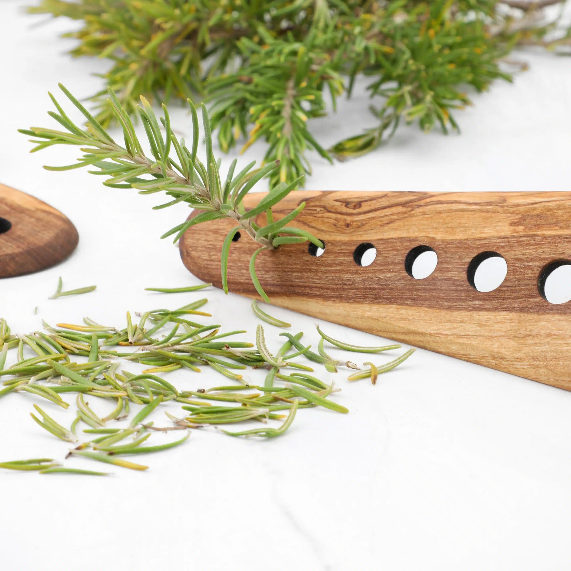 Multifunctional Wooden Herb Stripper from Olive Wood with 8 different-sized holes, presented on a white surface; this tool's robust build and hand-finished touch make it a unique gift for food lovers and a staple in any cook’s collection.